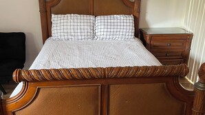 Una cama de madera con cabecera, una mesita de noche y otra mesilla auxiliar.