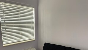 Una habitación con un sofá negro, una ventana con persianas y un aire acondicionado instalado en la pared.
