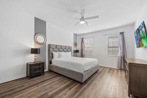 A bedroom with a bed, a nightstand, a ceiling fan, a window with blinds, and a wall-mounted TV. - Arcade, Waterpark, Theater, LEGO Room, Pool & Spa, Dual 86” TVs: Paradise Palms (Davenport)
