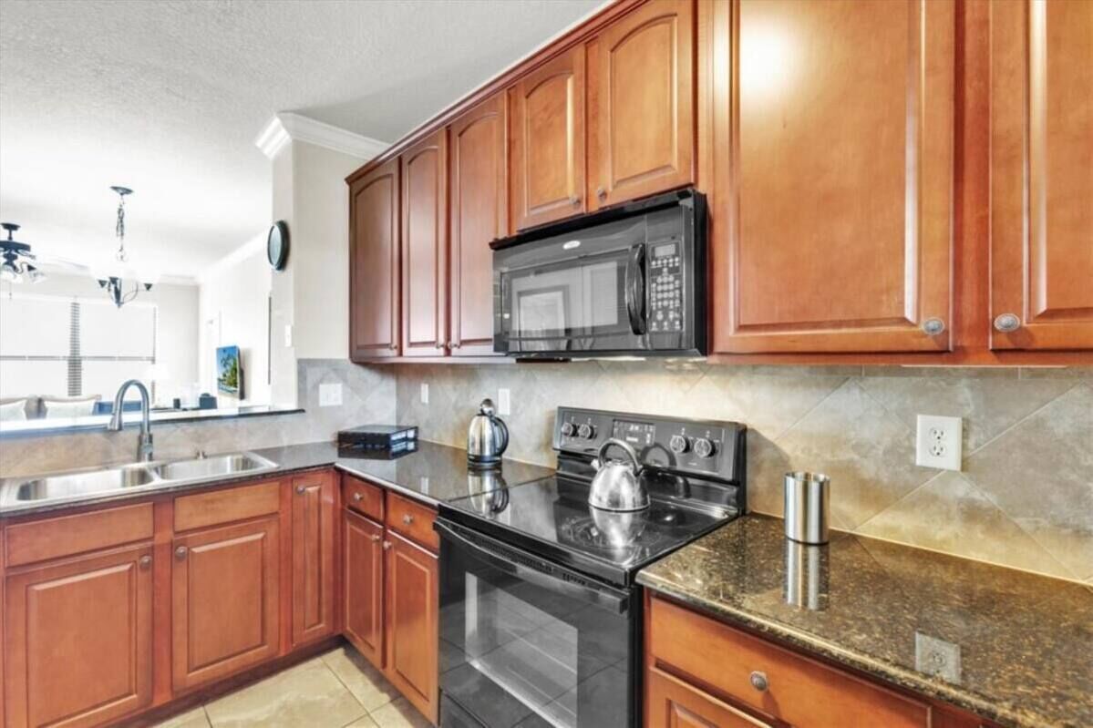 Una cocina con gabinetes de madera, un lavamanos de acero inoxidable, una estufa negra y un microondas.