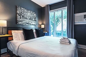 Quarto de hotel com uma cama grande, duas mesas de cabeceira, ar condicionado fixado na parede e uma janela com cortinas.