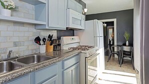 A kitchen with light blue cabinets, a granite countertop, a gas stove, a microwave, and a refrigerator.