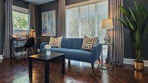 A living room with a blue sofa, a coffee table, a desk with a chair, a lamp, and a large plant.