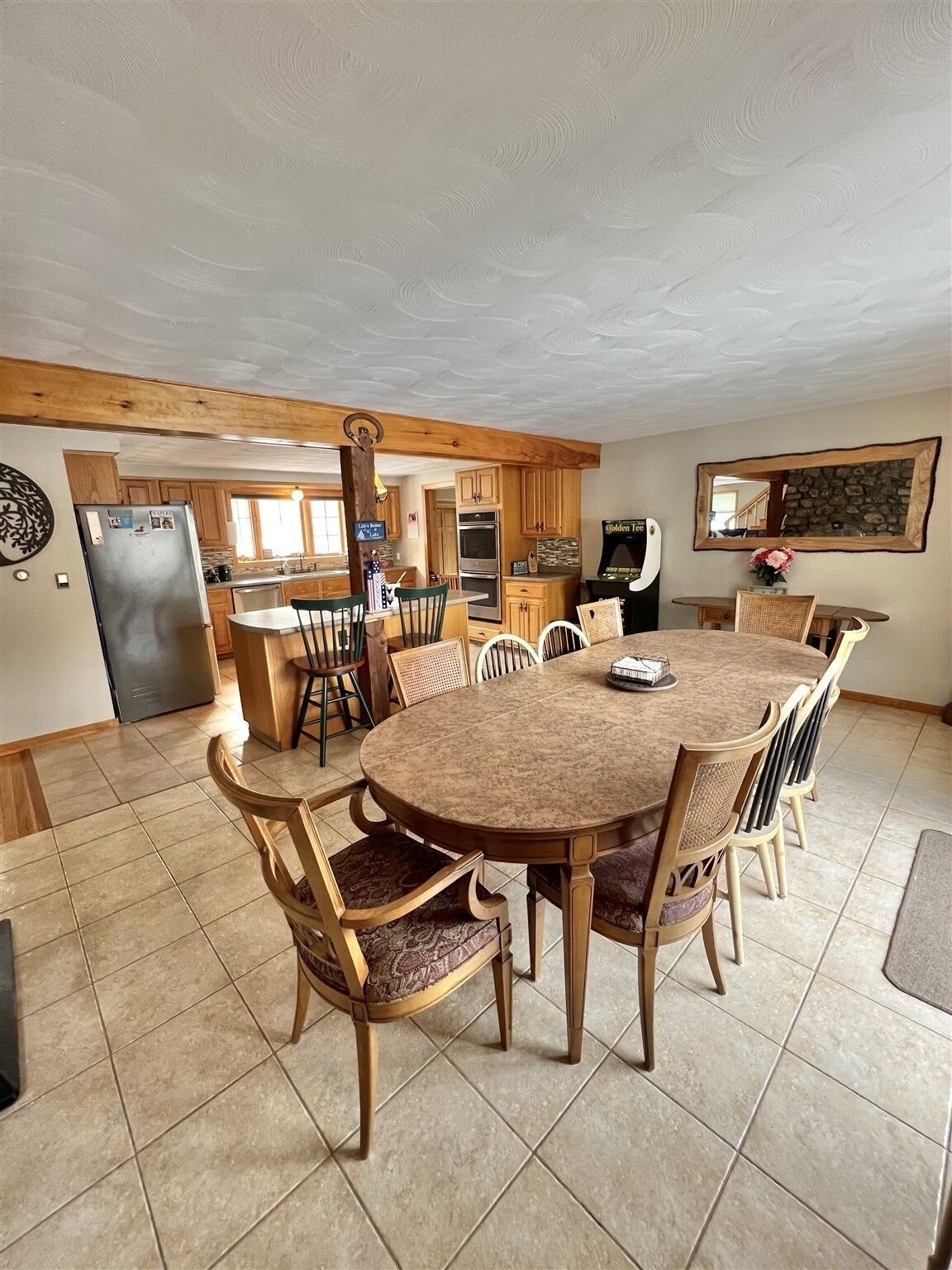 A spacious kitchen with a large dining table surrounded by chairs, wooden cabinets, and a refrigerator.