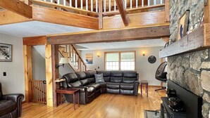 A spacious living area with a wooden floor, a stone fireplace, a leather sofa, and a staircase leading to an upper level. - Loons View Limit 20 5 Bedroom Home (Naples)