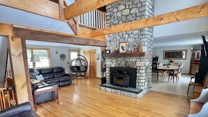 A spacious living area with a stone fireplace, wooden beams, and a high ceiling. - Loons View Limit 20 5 Bedroom Home (Naples)