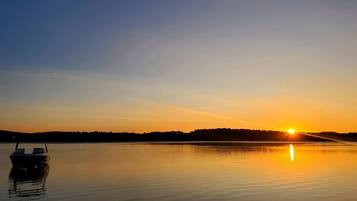 A calm lake at sunset with a boat in the foreground and a forested hill in the background.
