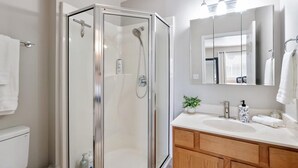 Un baño moderno con ducha de vidrio, un lavabo blanco, armarios de madera y un espejo grande.