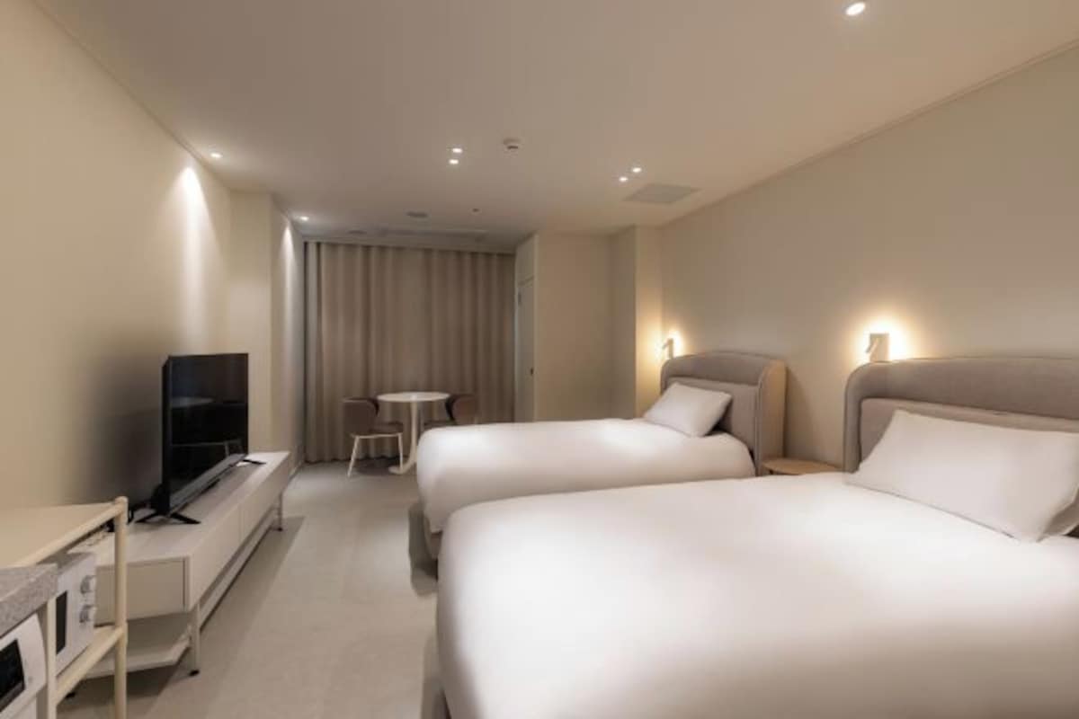 Une chambre d’hôtel avec deux lits, une télévision, une petite table et un rideau.