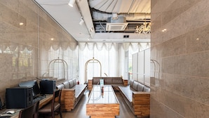 A modern lounge area with a long wooden table, cushioned seating, and a laptop on a desk.