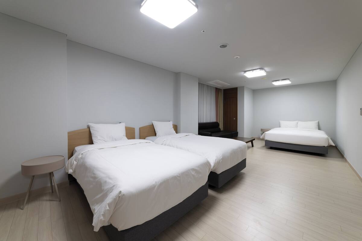 Una habitación de hotel moderna con dos camas grandes, una mesita redonda y un banco empotrado.