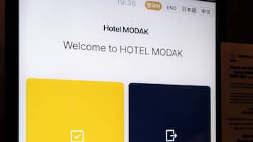 A digital display with a welcome message for Hotel MODAK, featuring a check-in interface with options for room selection.
