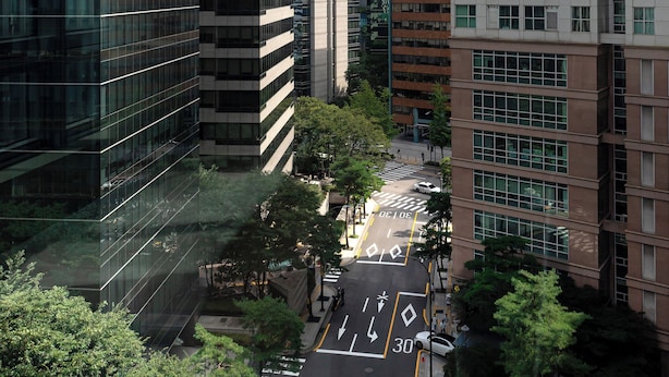 A modern urban street with tall buildings, a clear sky, and a road with directional arrows.