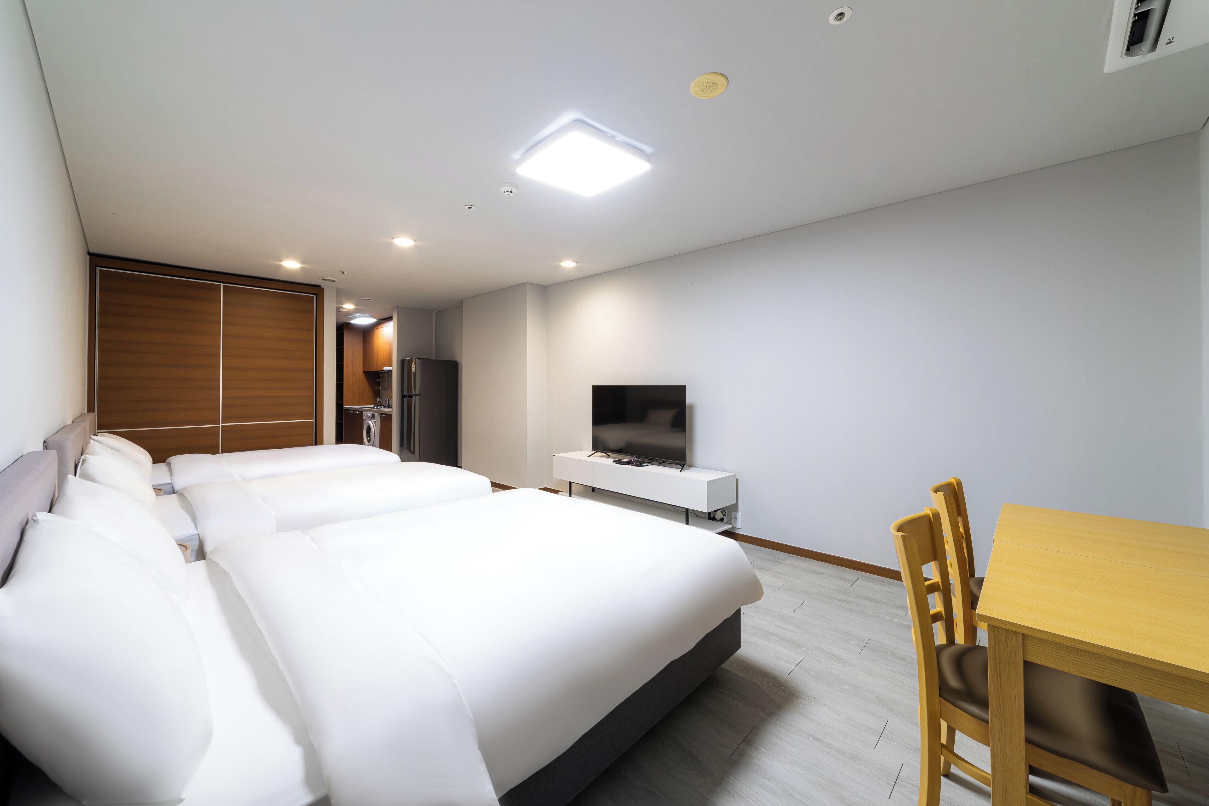 Une chambre d’hôtel avec un grand lit, une télévision, une table à manger en bois et un petit coin cuisine.