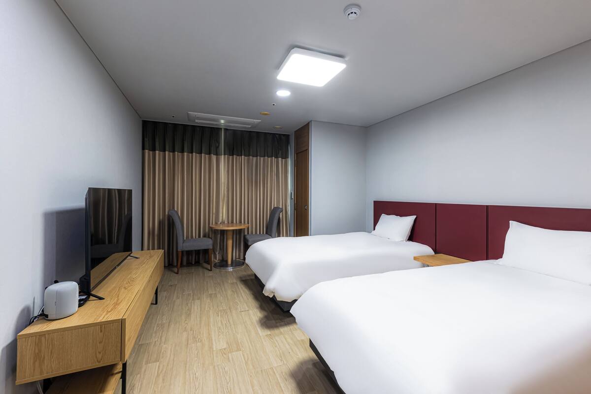 Habitación de hotel con dos camas, un escritorio, una silla, un televisor y una cortina.