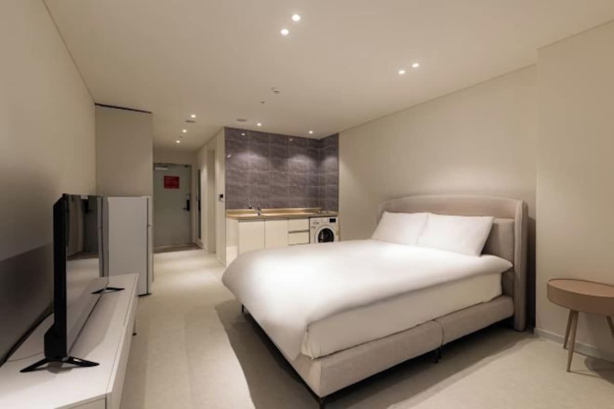 Une chambre d’hôtel moderne dotée d’un grand lit, d’un téléviseur à écran plat, d’une petite table et d’un lave-linge encastré.