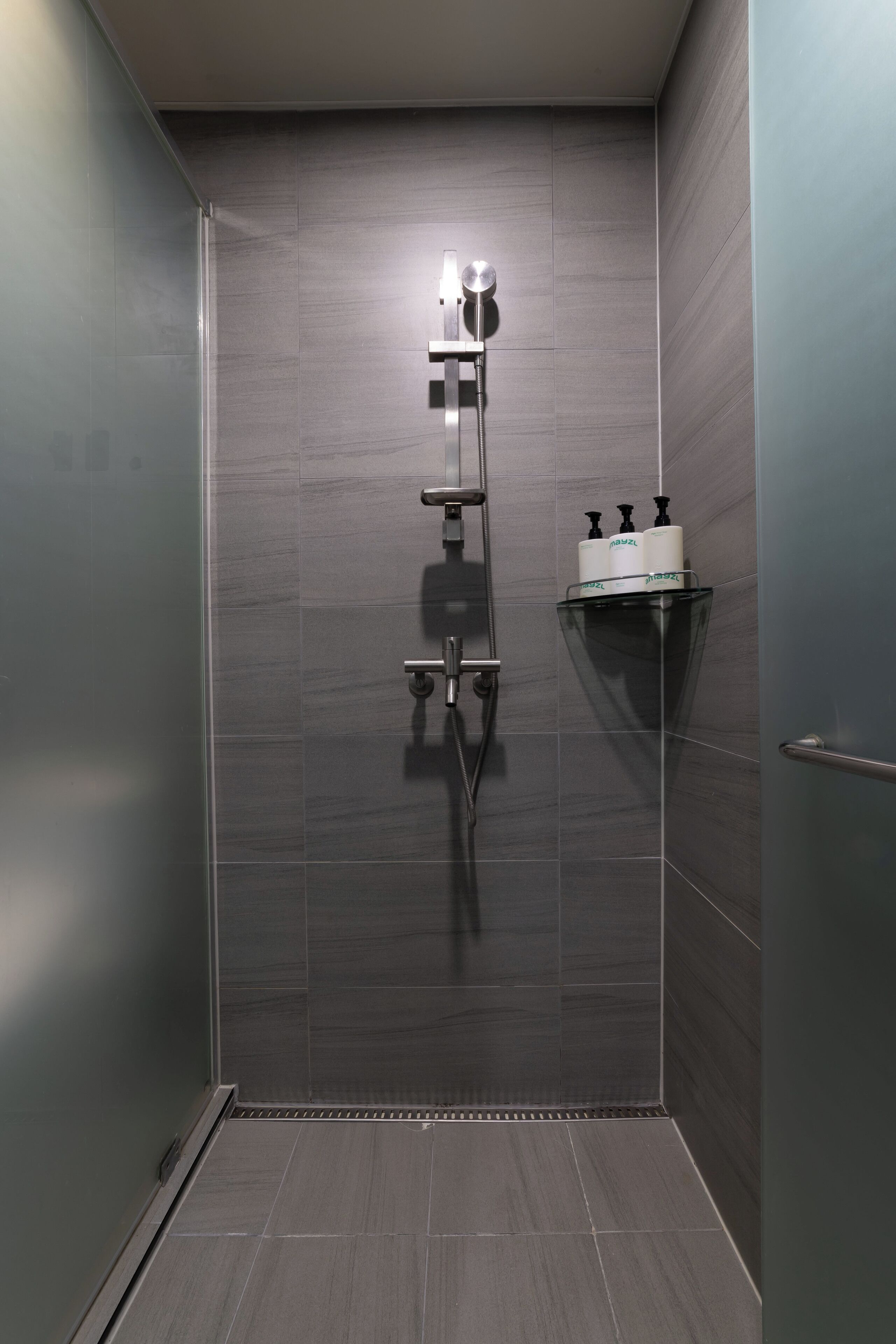 A modern shower with a glass enclosure, a wall-mounted shelf with toiletries, and a metallic handle.