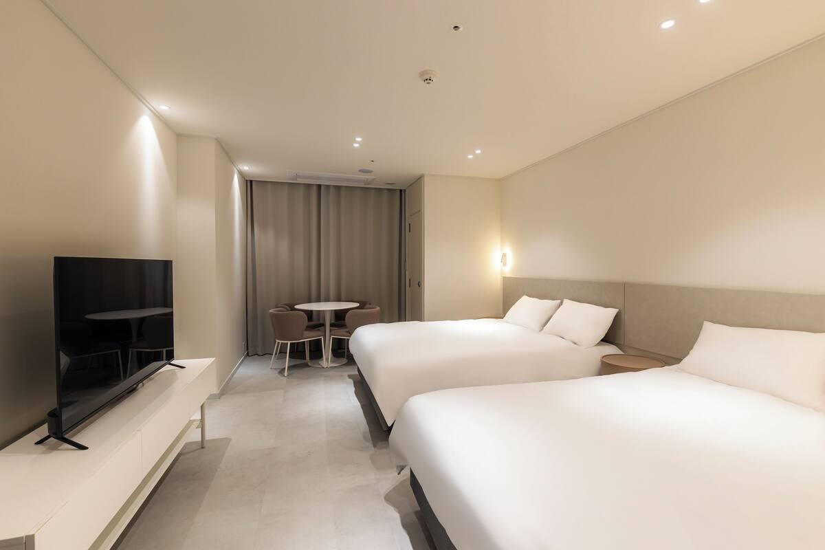 Una habitación de hotel moderna con dos camas, un televisor de pantalla plana, una mesita y una silla.
