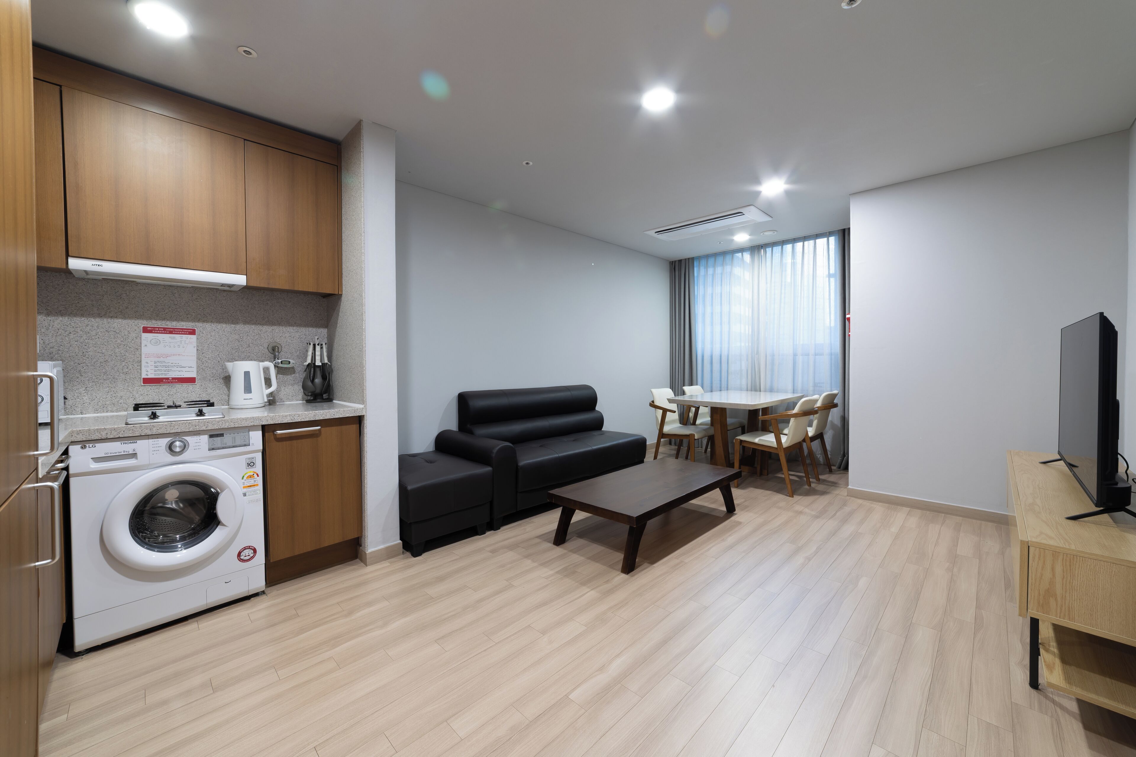 A modern apartment with a kitchen, a sofa, a dining area, and a TV.