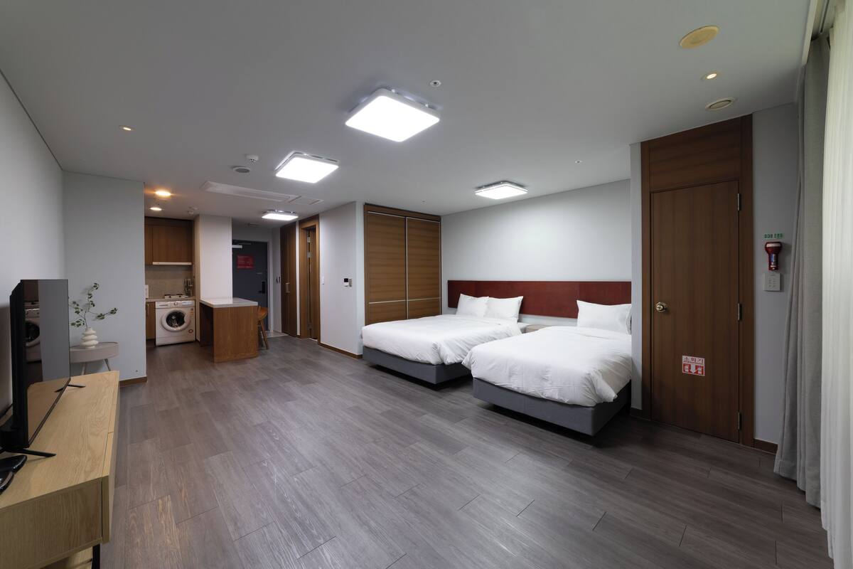 Habitación de hotel con dos camas, lavadora, escritorio con computadora y televisión.