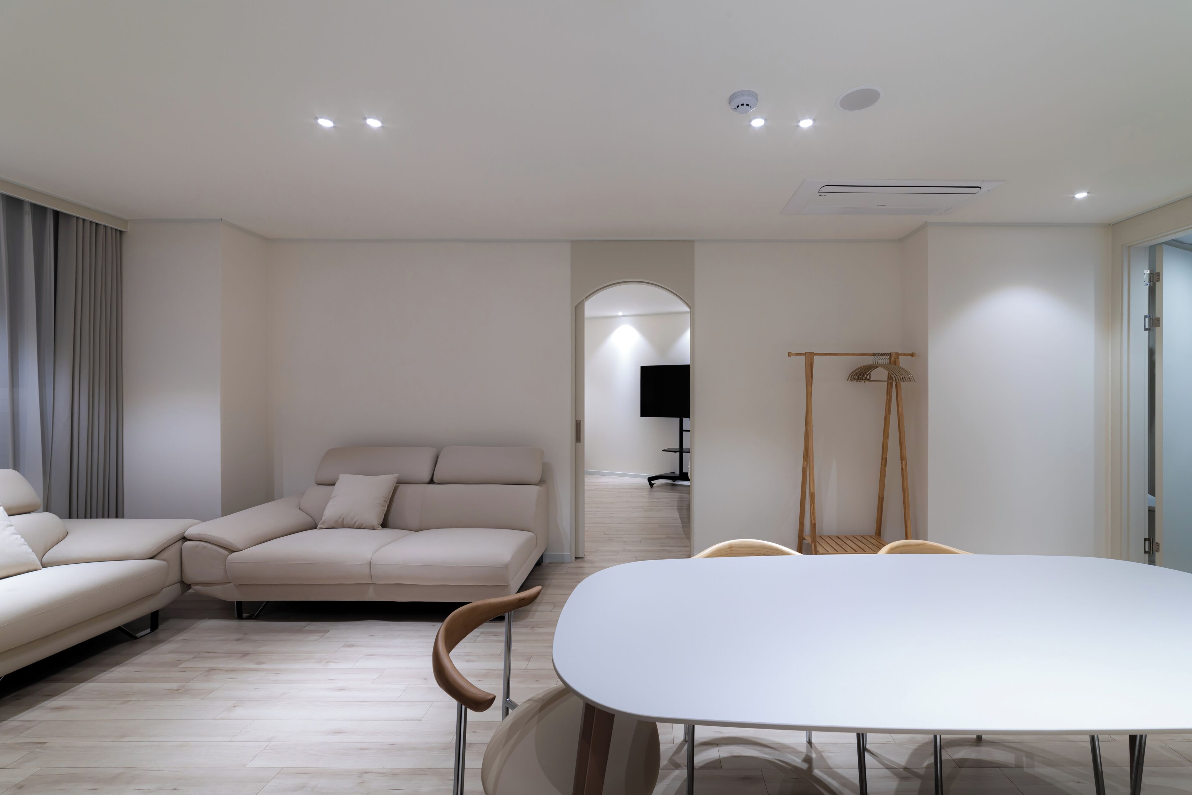A modern living room with a sofa, a dining table, and chairs. There is a TV in the background.