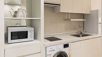 A compact kitchen with a built-in microwave, a washing machine, and a sink.