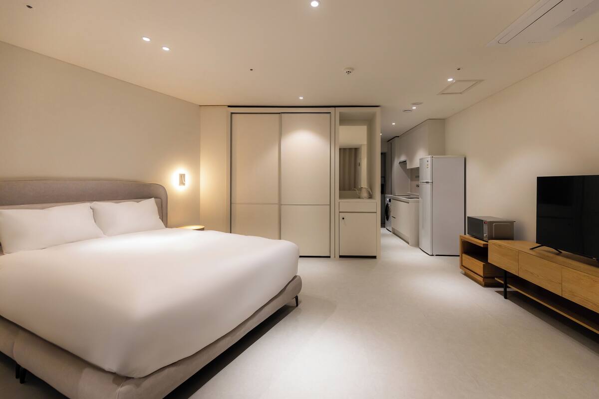 Una habitación de hotel moderna con una cama grande, televisión, armario y kitchenette.