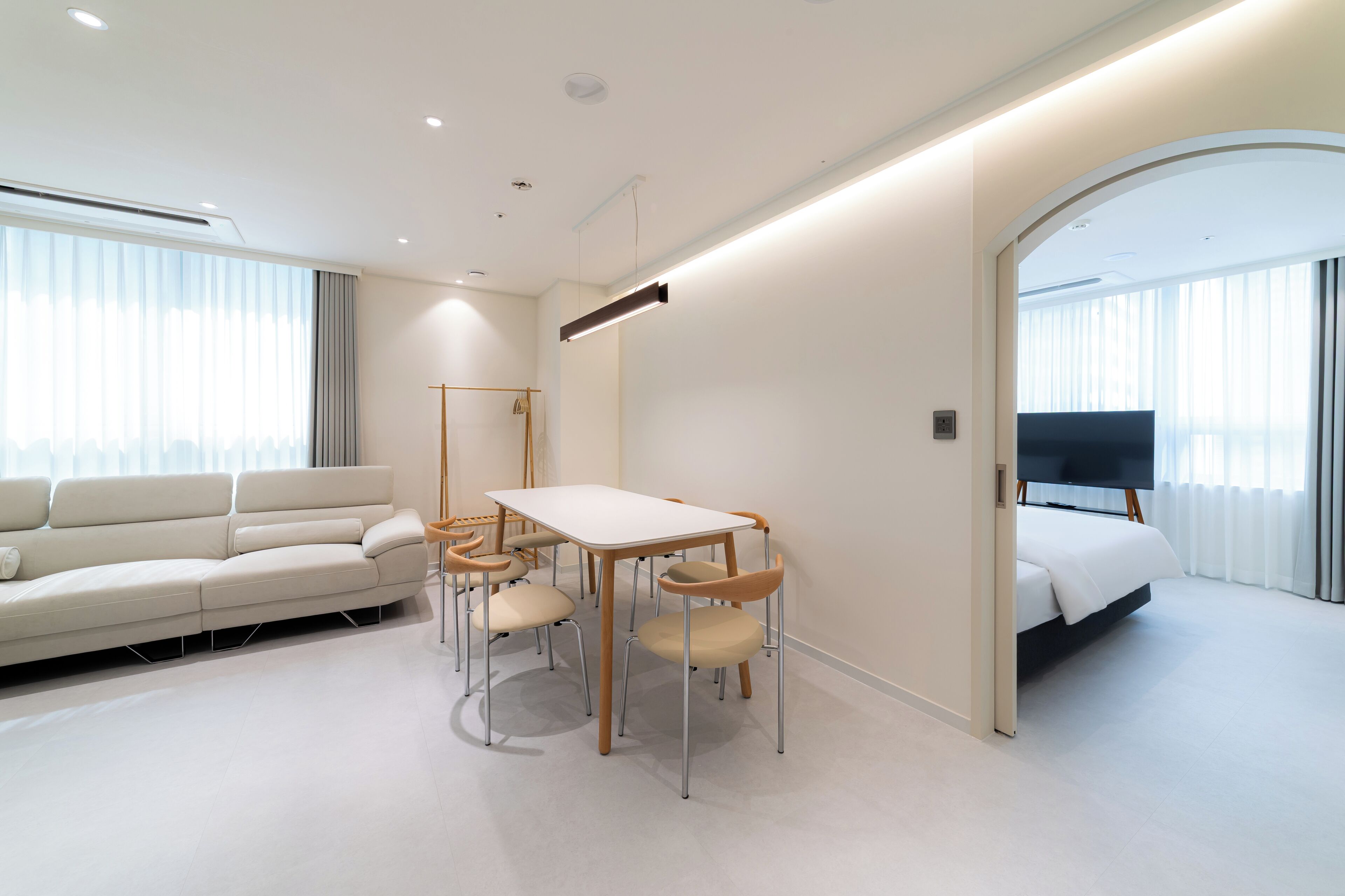 A modern hotel room with a sofa, a dining table with chairs, a bed, and a TV.