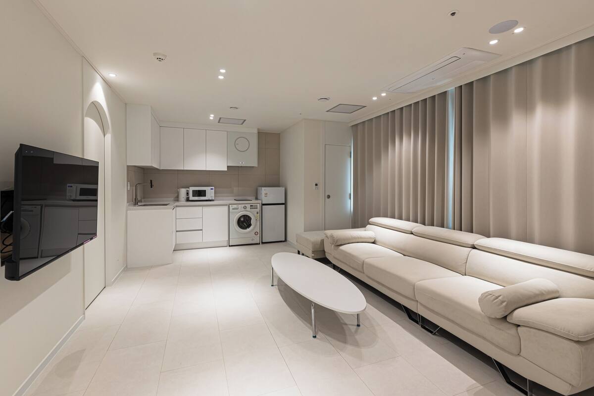 Una cocina moderna con electrodomésticos blancos, un comedor con mesa blanca y un sofá color beige.