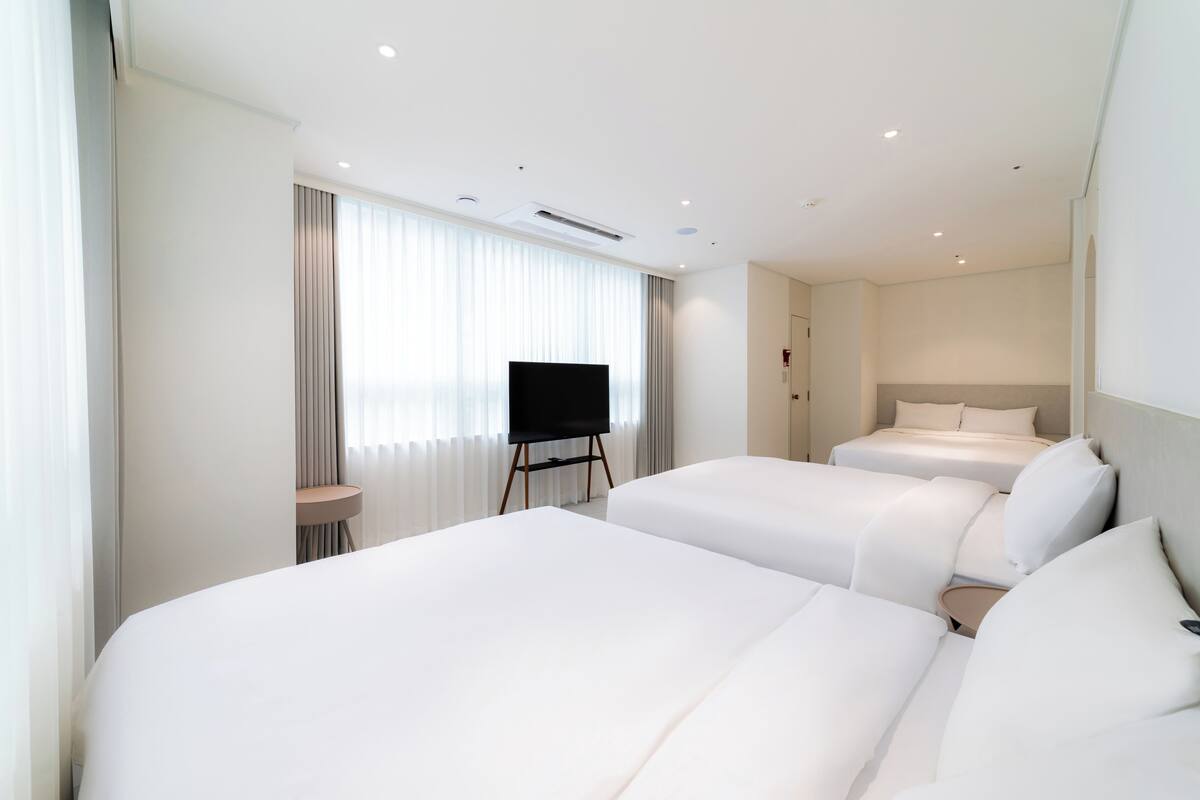 Habitación de hotel con dos camas, un televisor sobre un mueble bajo y un ventanal con cortinas.