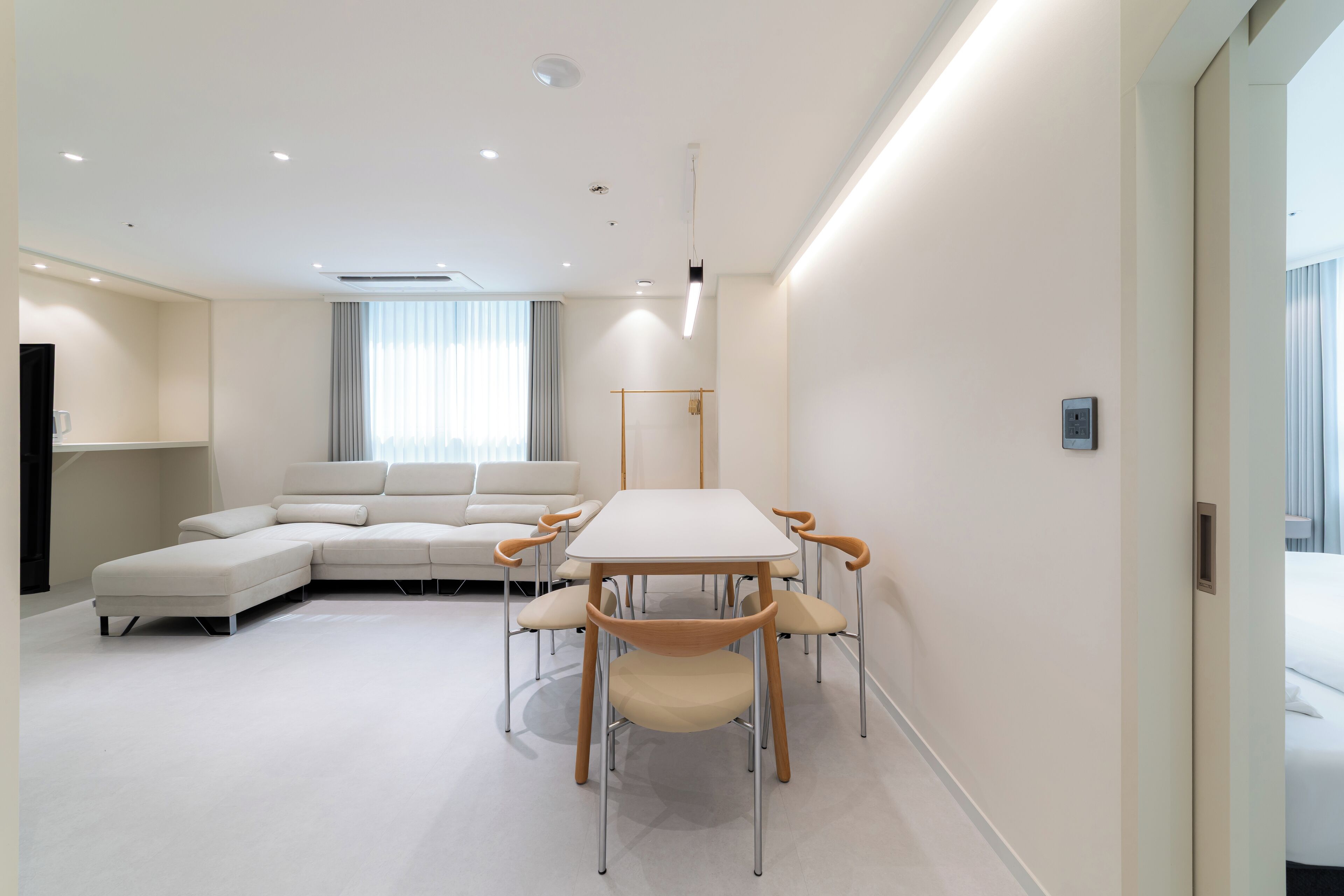 Ein modernes Hotelzimmer mit einer großen L-förmigen Couch, einem Esstisch mit sechs Stühlen und einem großen Fenster mit Vorhängen.