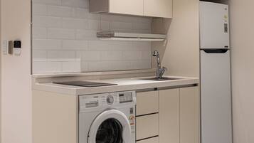 A compact kitchen with a built-in washer and dryer, a refrigerator, and a tiled backsplash.