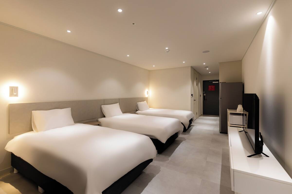 Habitación de hotel con tres camas, un escritorio y una televisión.