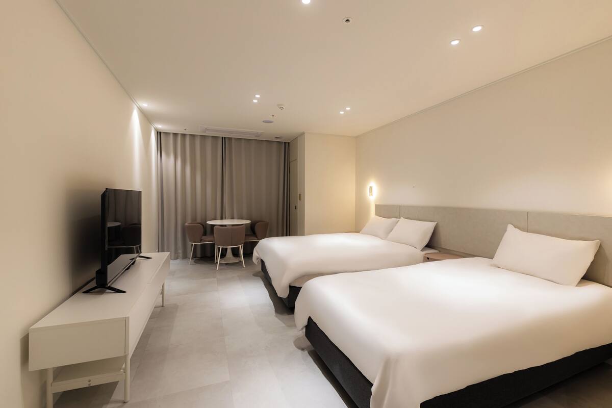Habitación de hotel con dos camas, un escritorio, una silla, un televisor y una ventana con cortinas.