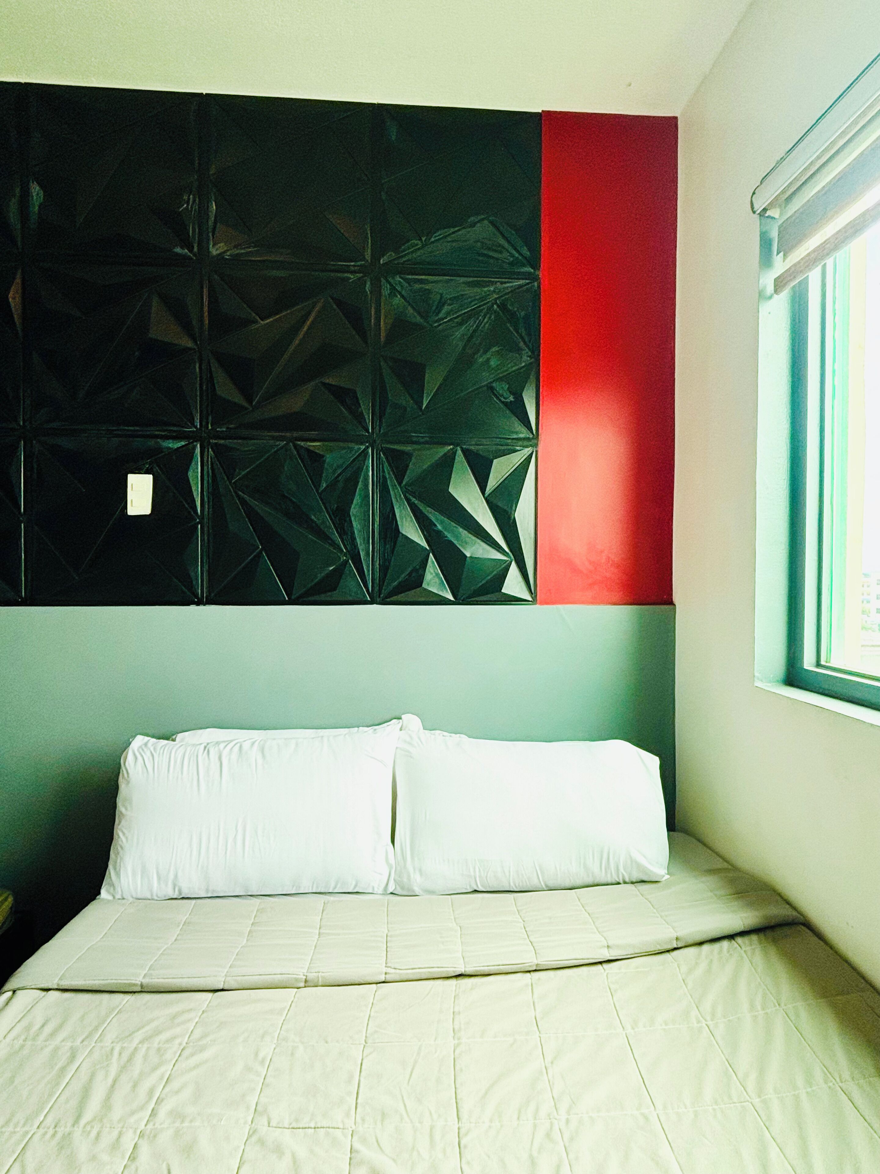 A bed with white bedding, a geometric wall panel, and a window with blinds.