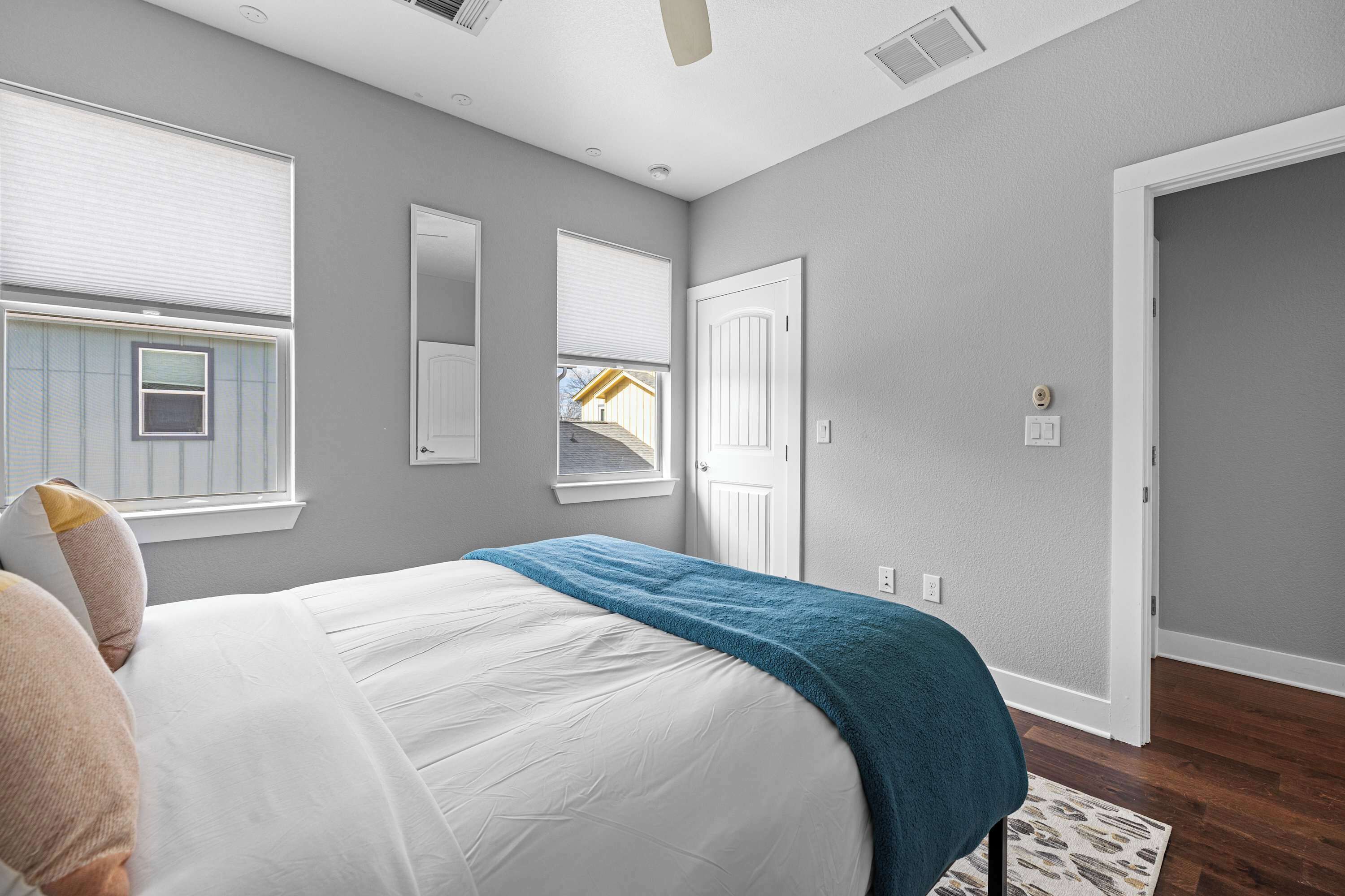 A bedroom with a bed, a window, a door, and a ceiling fan.