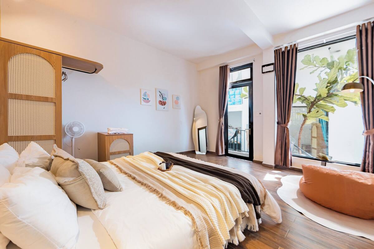 A modern bedroom with a large bed, a bedside table, a fan, and a view of the outdoors.