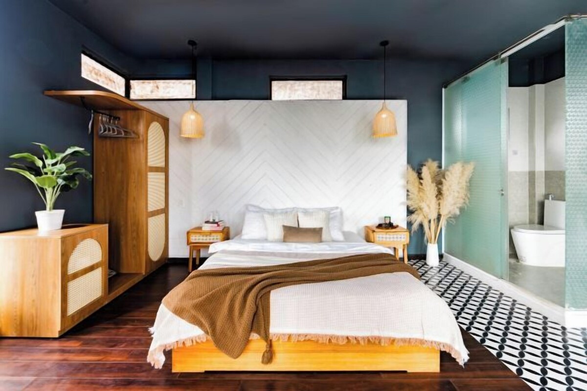 Une chambre à coucher moderne avec un grand lit, une commode en bois, des luminaires suspendus et une vue sur la salle de bain.