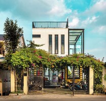 Um edifício moderno com fachada de vidro, entrada coberta com vegetação e o número
