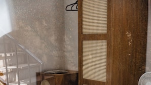 A bedroom with a bed, a wooden wardrobe, a white fan, and a staircase.