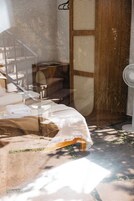 Quarto com uma cama, um guarda-roupa de madeira, um ventilador branco e uma escada.
