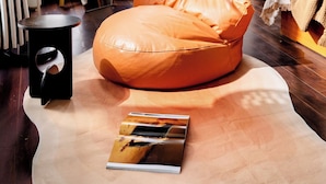 A room with a large window, a bean bag chair, a small table with a lamp, and a potted plant.