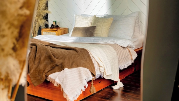 A modern bedroom with a herringbone-patterned headboard, a wooden nightstand, a hanging lamp, and a bed with multiple pillows and a blanket.