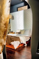 Quarto moderno com cabeceira em padrão herringbone, mesa de cabeceira de madeira, luminária pendente e cama com várias almofadas e cobertor.