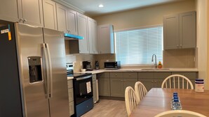 A modern kitchen with stainless steel appliances, a dining area with a wooden table and chairs, and a window with blinds. - 1280A - 2-bedroom/2 bathrooms in Pasadena (Pasadena)