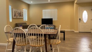 A dining area with a wooden table and white chairs, a gray sofa, and a painting on the wall. - 1280A - 2-bedroom/2 bathrooms in Pasadena (Pasadena)
