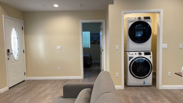 A laundry room with two stacked washers and dryers, a gray sofa, and a door with a glass window. - 1280A - 2-bedroom/2 bathrooms in Pasadena (Pasadena)