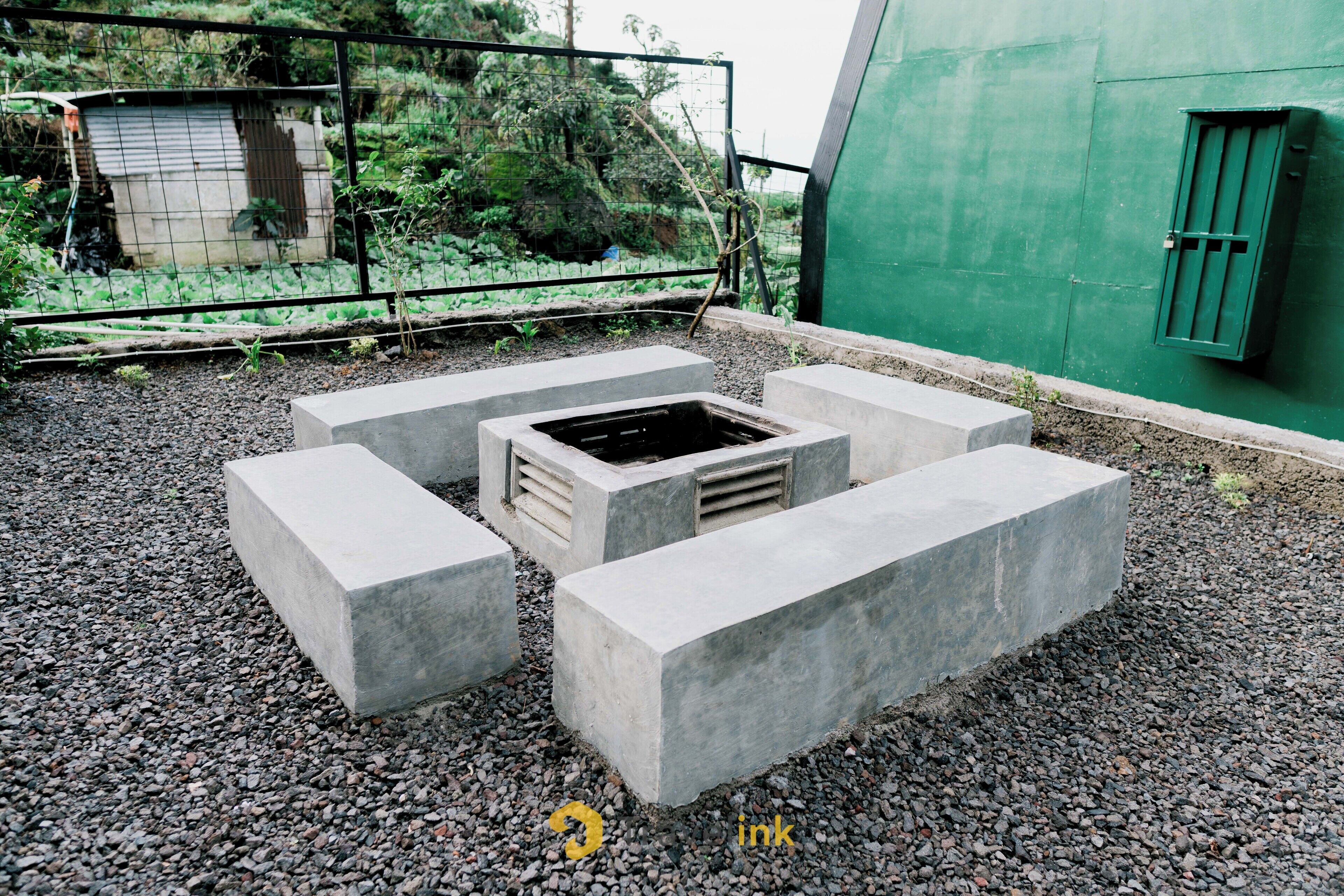 Un área de estar exterior de concreto con un brasero central, rodeado de losas de piedra.