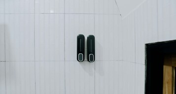 Una pared de azulejos blancos con dos objetos negros sujetos a ella.