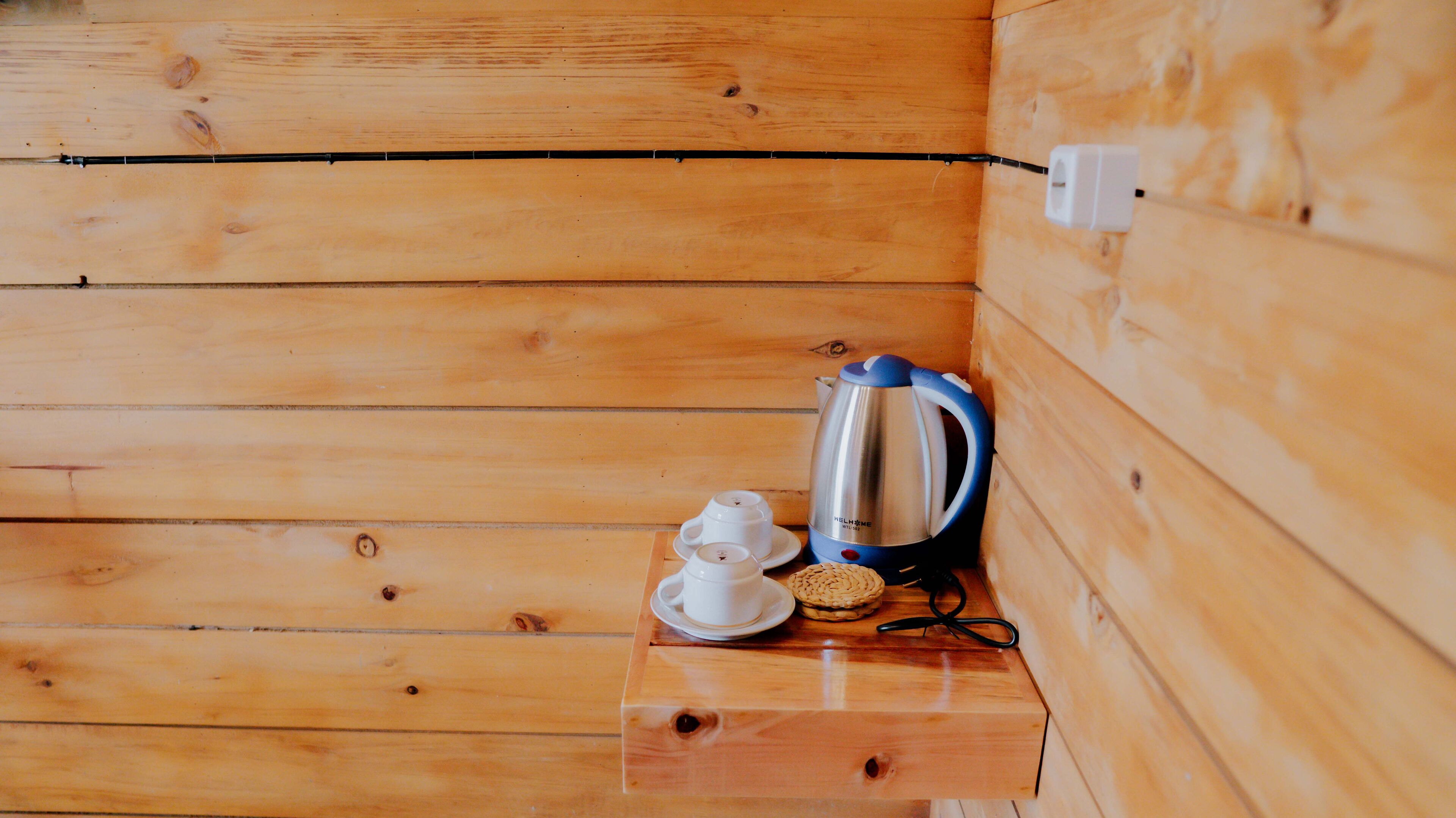Een houten interieur met een kleine tafel waarop een waterkoker, twee kopjes en een bord staan.